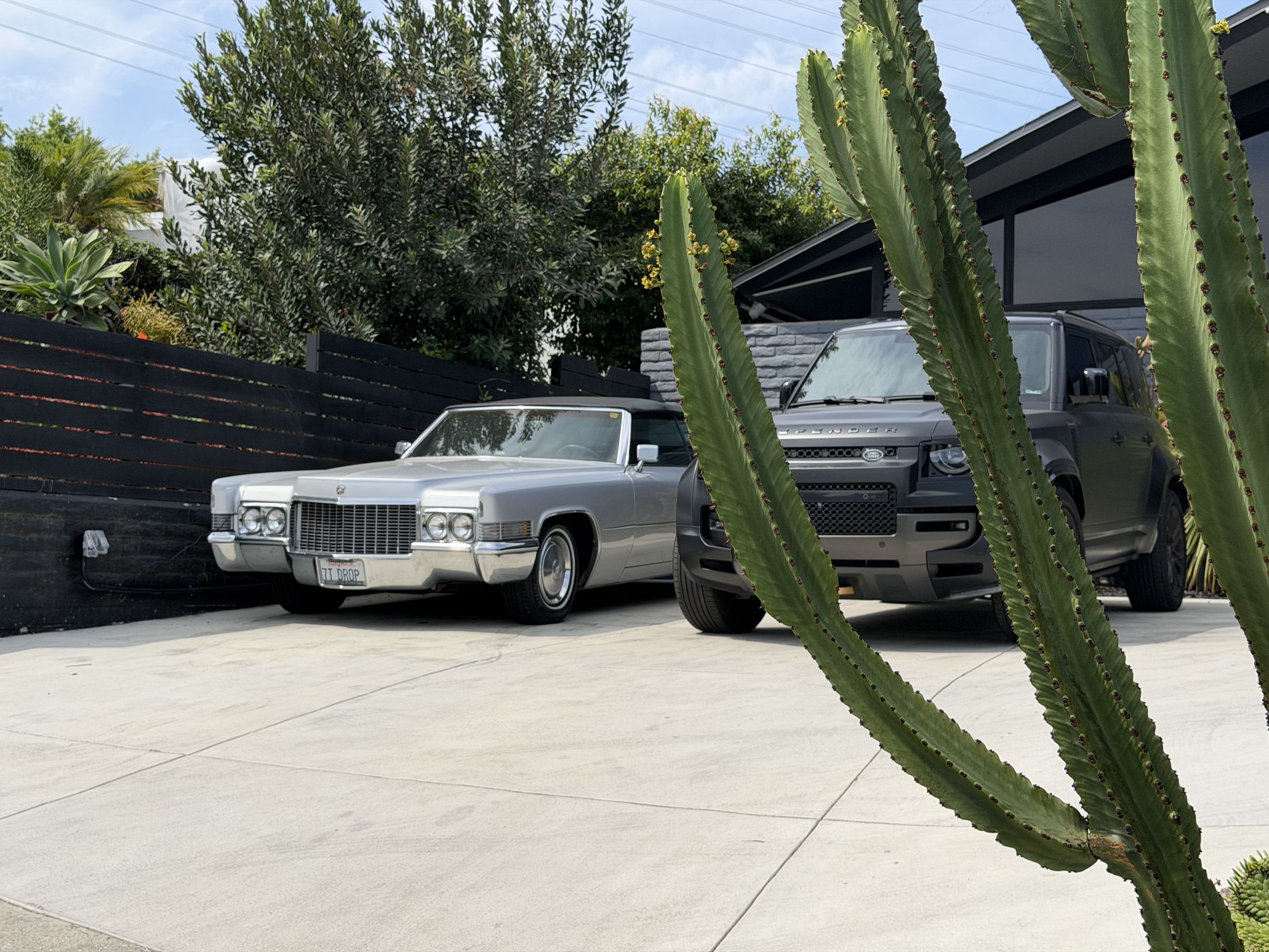 A silver vintage Cadillac convertible parked beside a four-wheel drive, framed by cactus