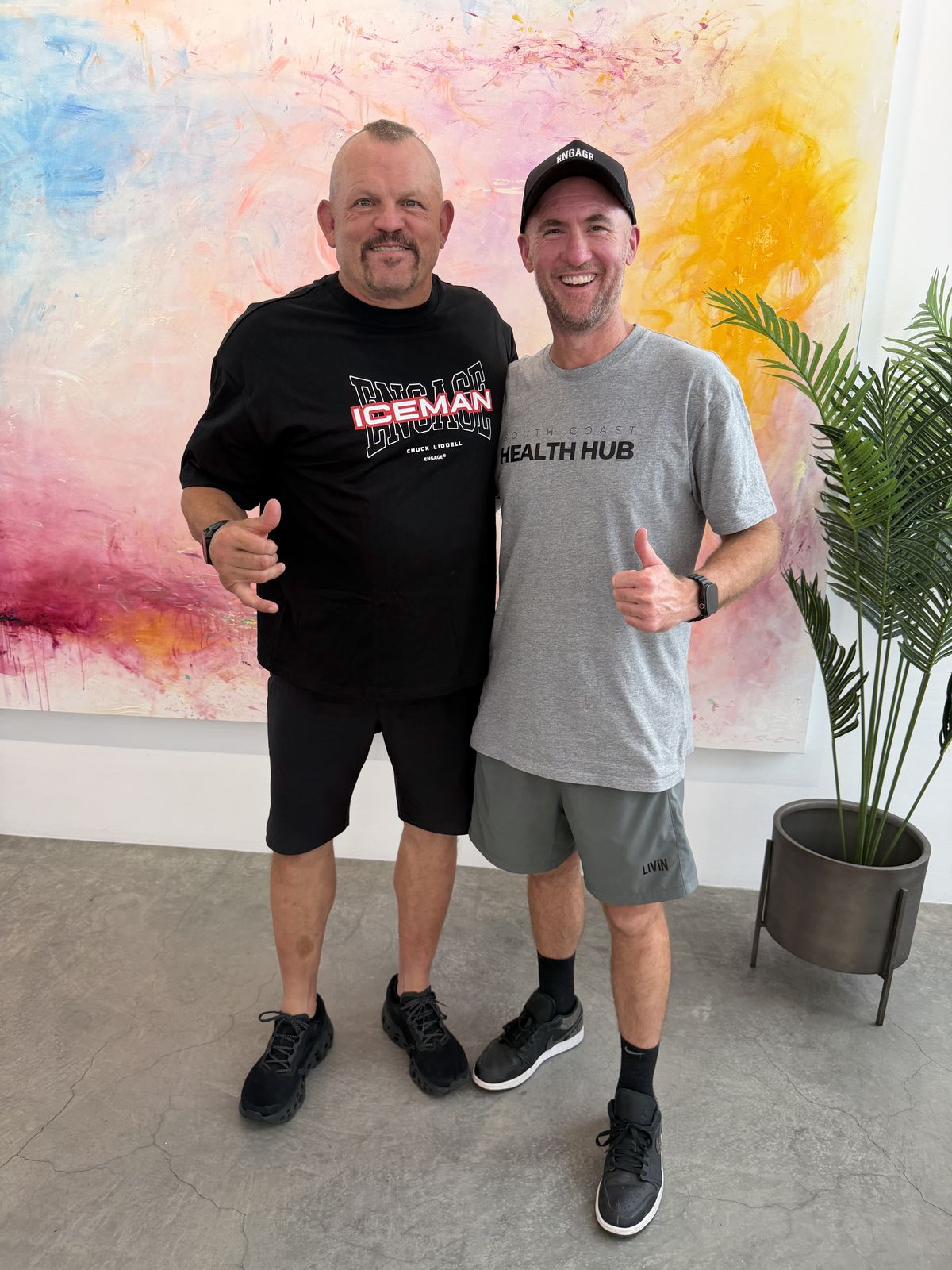Mick Baines standing with Chuck Liddell in front of a large painted canvas