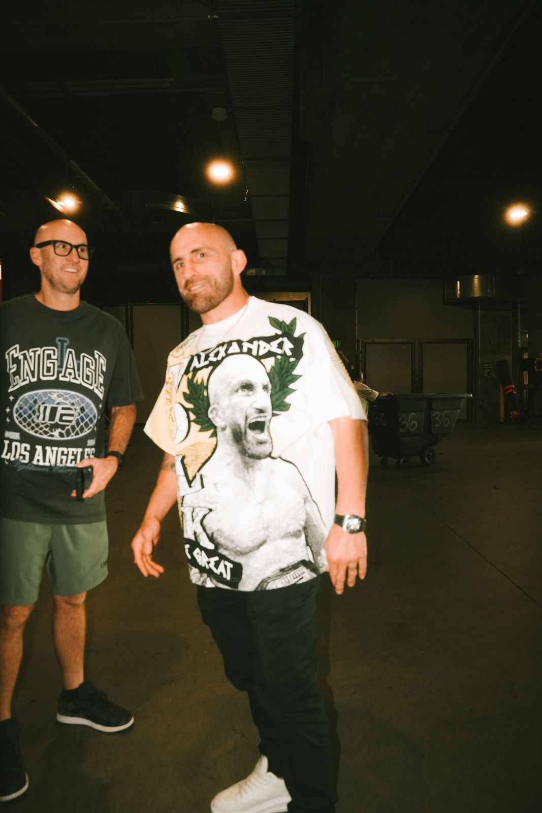 Two men in Engage and Volk shirts walking through a darkened venue