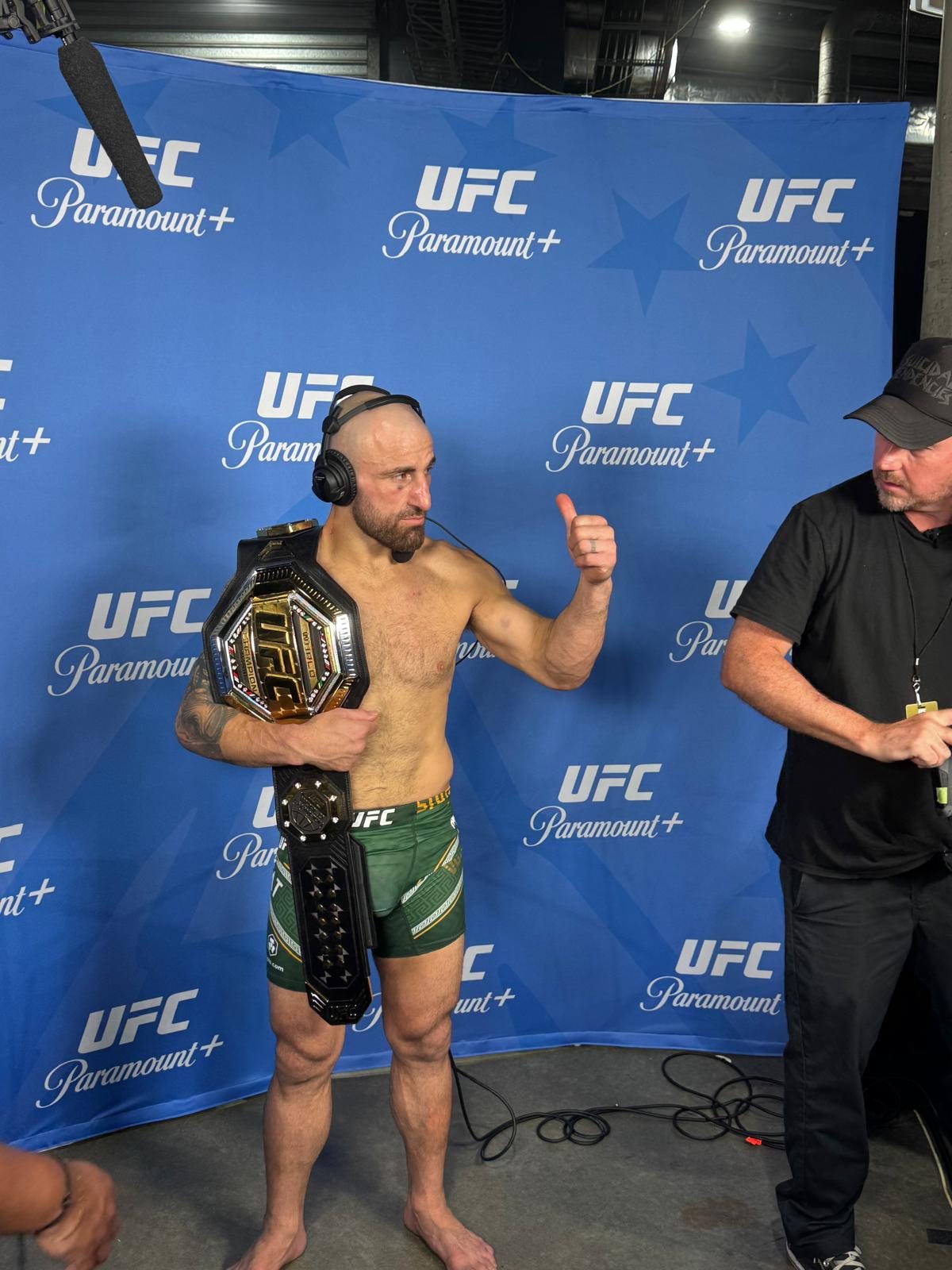 Volk with the belt on the UFC backdrop.