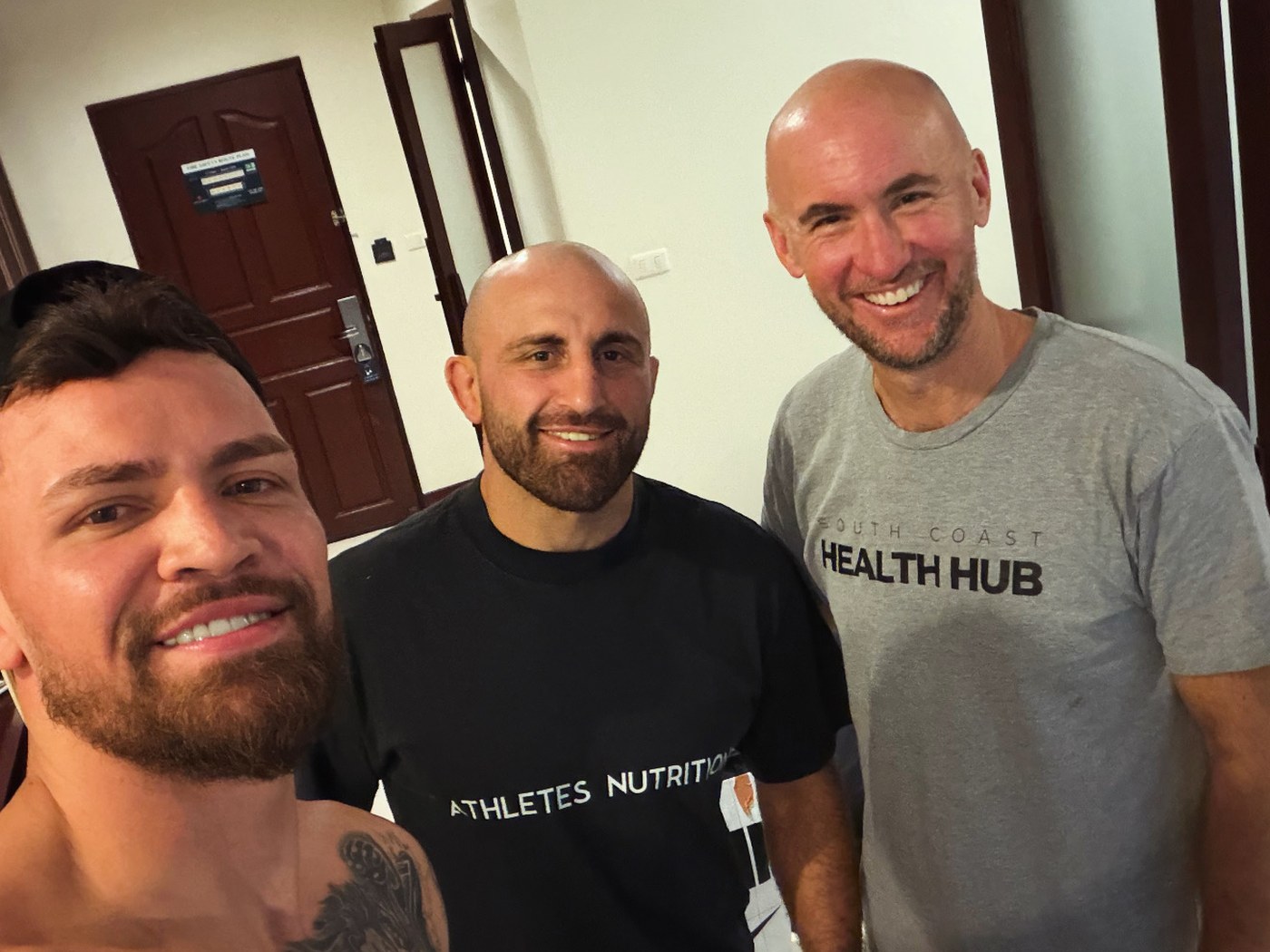 Three men standing together in a hotel corridor, one wearing a South Coast Health Hub shirt