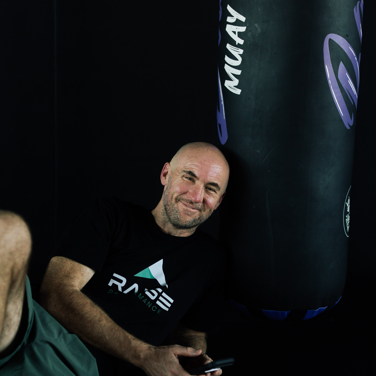 A man resting beside the Muay Thai bags