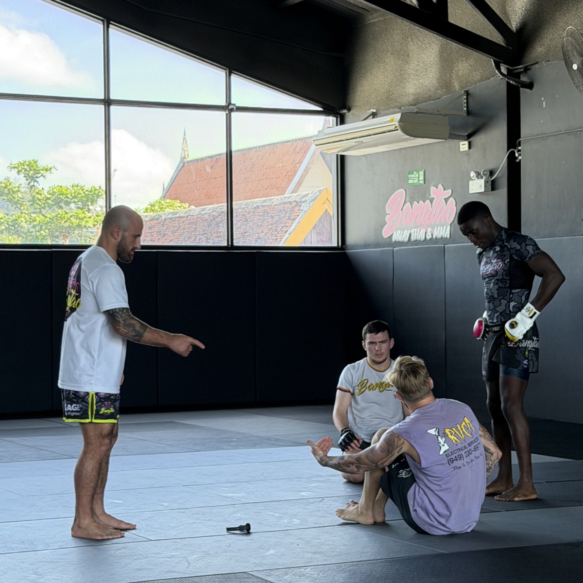 Four men on the mats at Bangtao Muay Thai and MMA, one standing and talking